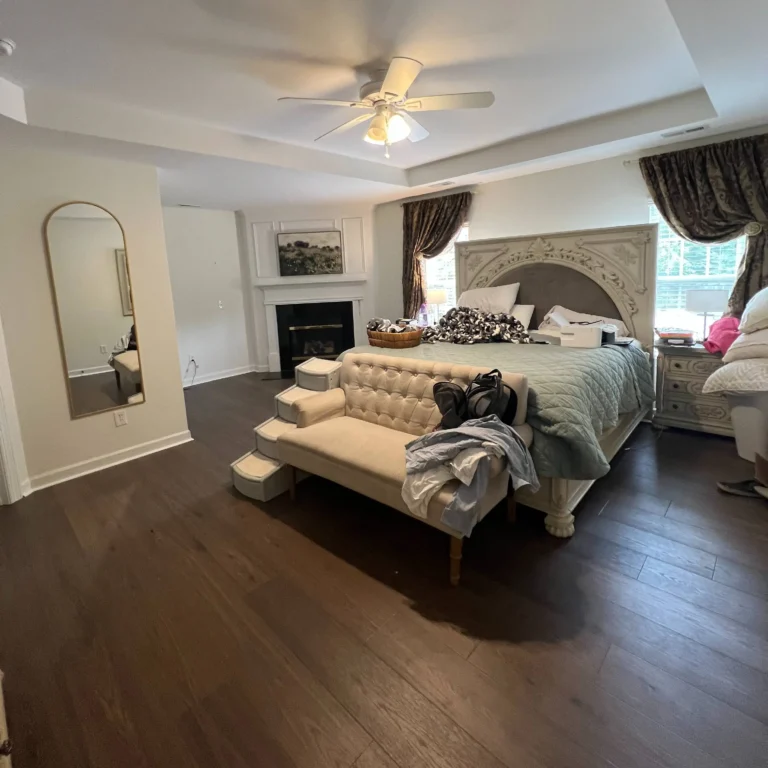 Newly renovated bedroom floors on dark wood color. A queen sized bed in the middle and a mirror on the left wall